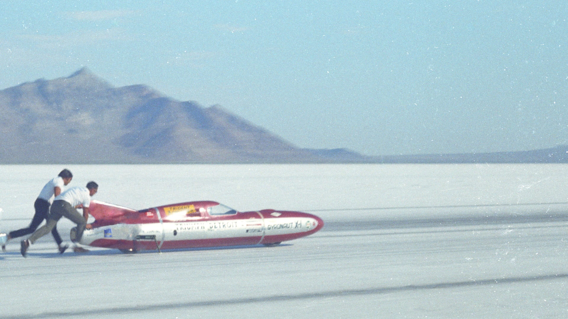 Two people steering the Castrol Rocket into position on a sandy plain